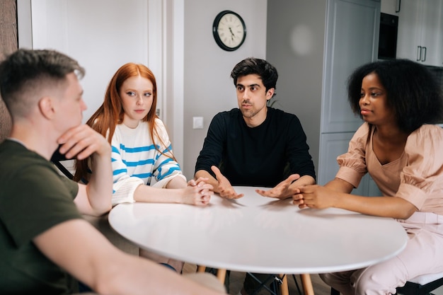 Groep ontspannen diverse mensen die aan een cirkeltafel in de woonkamer zitten en met elkaar communiceren tijdens een ontmoeting in een stijlvolle woonkamer