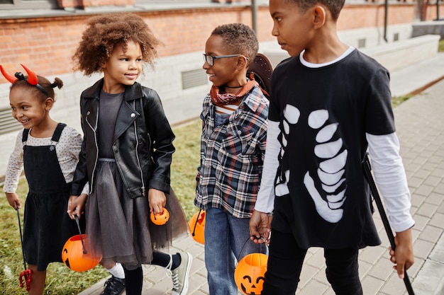 Groep opgewonden Afro-Amerikaanse kinderen die buiten Halloween-kostuums dragen terwijl ze trick or treat...