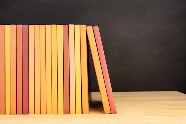 Groep oranje boeken op houten tafel of planken en schoolbord op de achtergrond. ruimte kopiëren