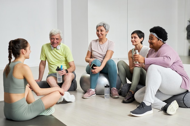 Groep ouderen die water drinken en rusten na training samen met coach