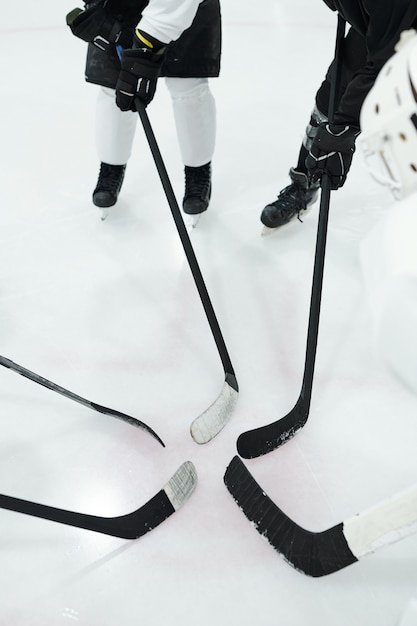 Groep professionele hockeyspelers in sportuniform, handschoenen en schaatsen die in een cirkel op de ijsbaan staan en hun stokken in het midden houden