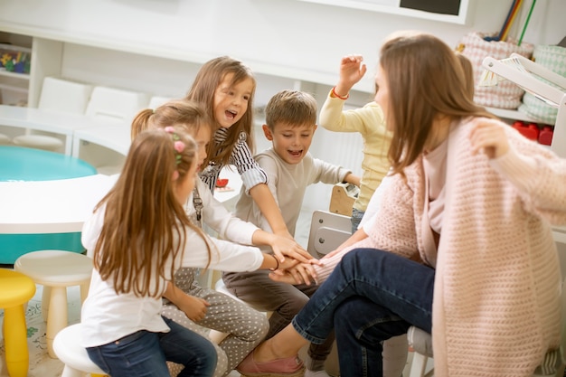 Groep schattige kleuters slaan de handen in elkaar met hun kleuterjuf