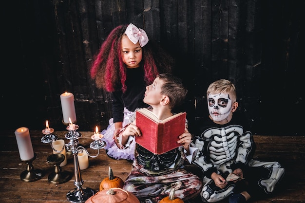 Groep schattige multiraciale kinderen in enge kostuums die horrorverhalen lezen in een oud huis, tijdens Halloween-feest. Halloween-concept.