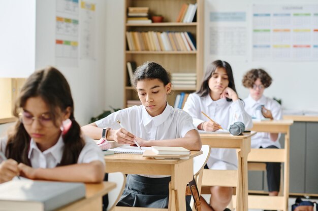 Groep schoolkinderen die aan bureaus zitten en aantekeningen maken in hun notitieboekjes tijdens de les op school