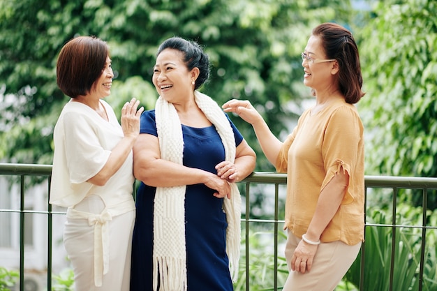 Groep senior Vietnamese vrouwelijke vrienden die op het balkon staan, nieuws bespreken en grappen maken