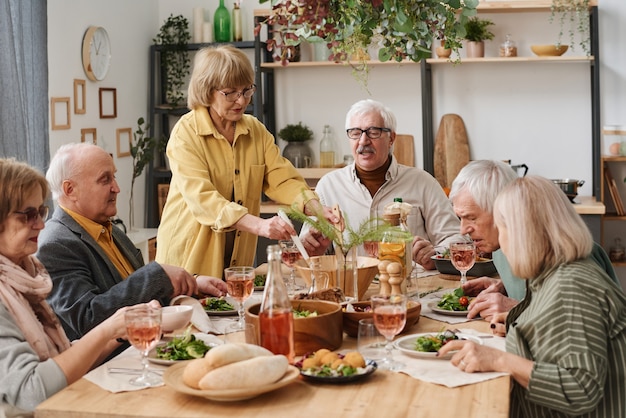 Groep senioren die aan de eettafel zitten te eten en thuis met elkaar te praten