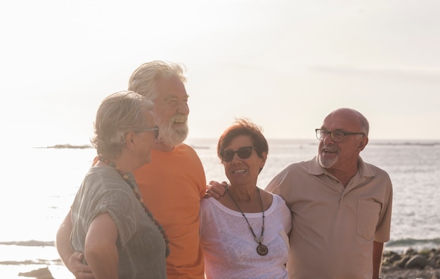 Groep senioren op het strand die samen praten en plezier hebben - gelukkige en volwassen paople in vriendschap of relatie met de zee of oceaan op de achtergrond