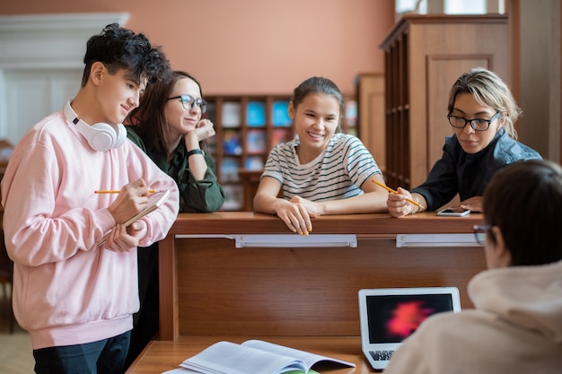 Groep slimme student die zich door programmeur voor laptop bevindt die hen helpt om informatie voor seminarie te vinden