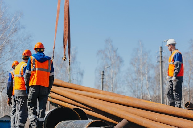 Groep slingers in bouwhelmen en vesten op straat lossen metalen buizen Echte scène