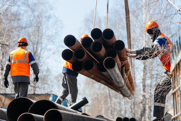 Groep slingers in bouwhelmen en vesten op straat lossen metalen buizen Echte scène