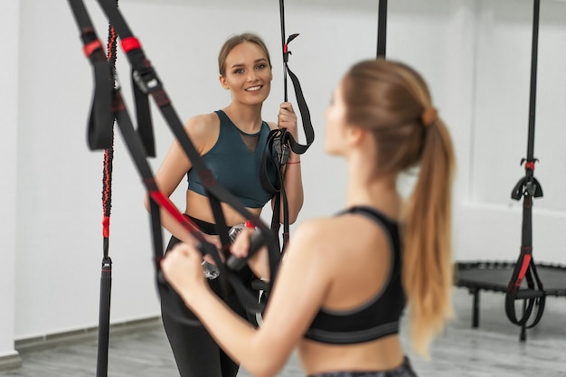 Groep sportieve vrouwen die trainen met trx-fitnessapparatuur met trainer in de buurt