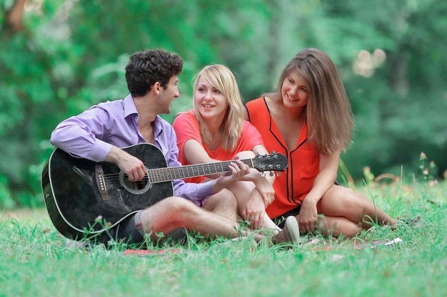 Groep studenten met een gitaar ontspannen zittend op het gras in het stadspark.