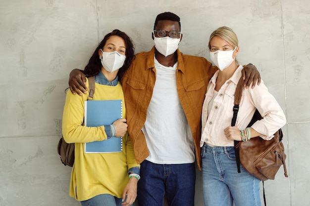 Groep studenten omarmen terwijl ze beschermende gezichtsmaskers dragen en tegen de muur staan in de gang van de universiteit.