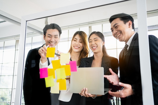 Groep succesvolle Aziatische zakenlieden en vrouwen teamwork Brainstormvergadering met plaknotities op de glazen wand voor nieuwe ideeën Agile methodologie gebruiken voor zaken in een tech startup-kantoor