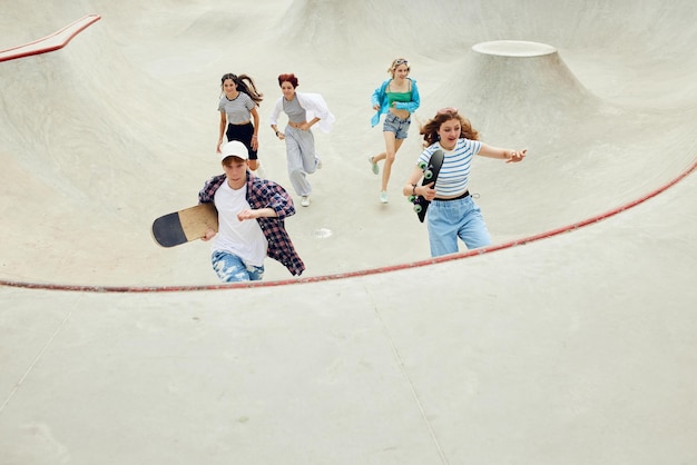 Groep tieners in vrijetijdskleding jongen en meisjes rennen met skate op skateboardhelling Activiteit en plezier Concept van jeugdcultuur sport dynamische extreme hobby actie en bewegingen vriendschap