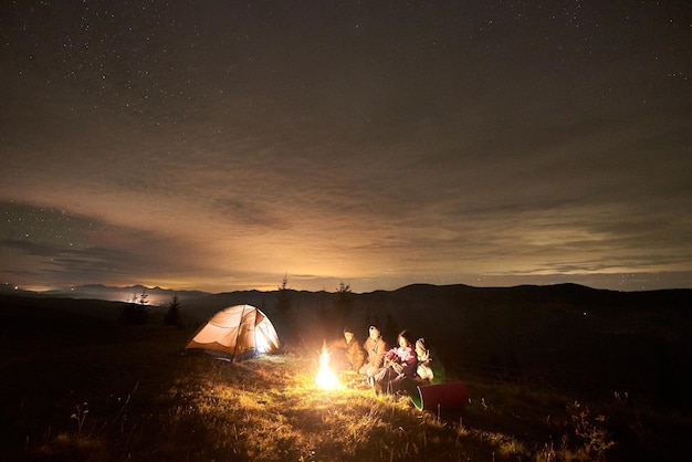 Groep toeristen met gitaar door vreugdevuur te branden onder de donkere sterrenhemel met het sterrenbeeld Melkweg.