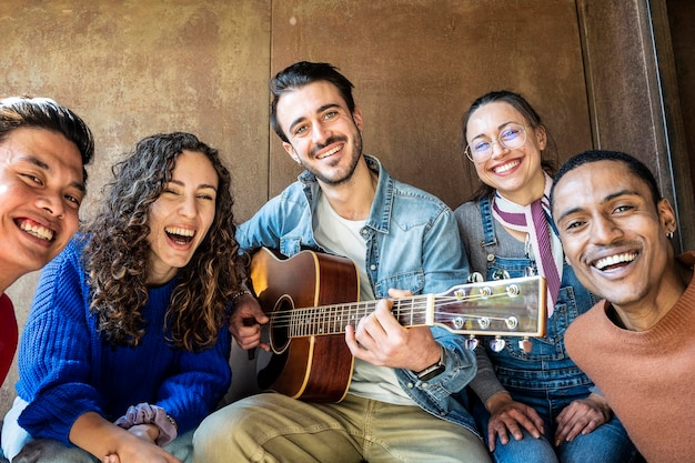 Groep trendy multi-etnische studenten die samen plezier hebben op de universiteit van de vrijetijdsruimte gelukkige jonge mensen genieten van tijd om muziek te spelen en samen te lachen