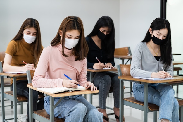 Groep universiteitsstudenten die een gezichtsmasker dragen en afstand houden tijdens het studeren in de klas en de universiteits- of universiteitscampus om de covid-19-pandemie te voorkomen. het nieuwe leven op de hogeschool of universiteitscampus