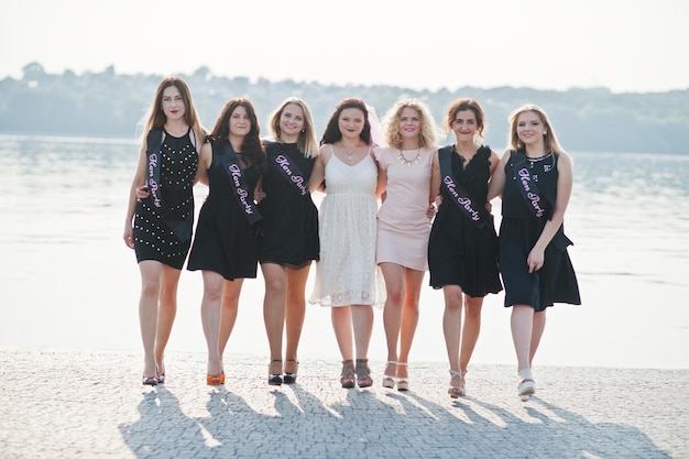 Foto groep van 7 meisjes dragen op zwart en 2 bruiden op vrijgezellenfeest tegen zonnig strand