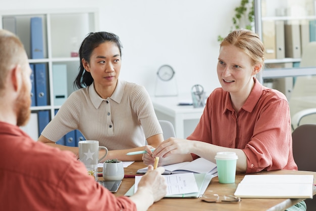 Groep van collega's aan de tafel zitten en met elkaar praten tijdens zakelijke bijeenkomst op kantoor