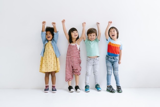 Groep van diverse etniciteit Kleine kinderen die hun handen omhoog steken en glimlachen Geïsoleerd op grijze achtergrond Jeugd vrijheid geluk actieve levensstijl concept