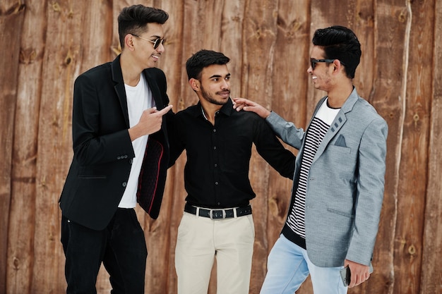 Groep van drie casual jonge indiaan mans poseerde tegen houten achtergrond