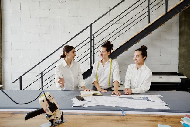 Groep van drie jonge modeontwerpers in witte shirts brainstormen en ideeën voor nieuwe seizoenscollectie bespreken tijdens bijeenkomst