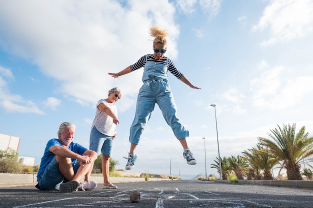 Groep van drie mensen van verschillende leeftijden die samen spelen op de hinkelbaan - volwassen man die op de grond zit - schoolspel en plezier hebben