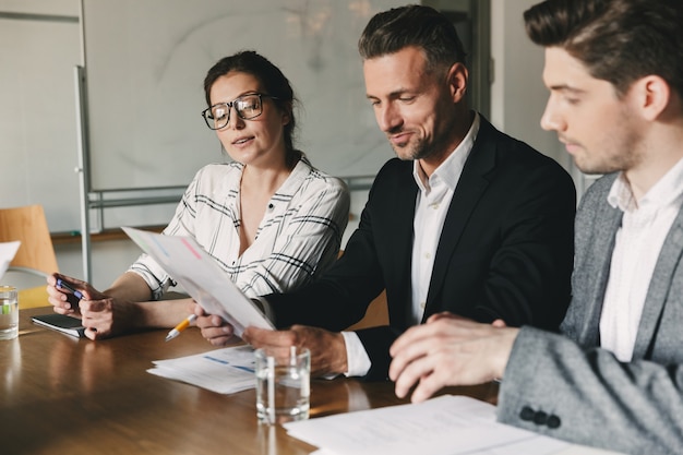 Groep van mensen uit het bedrijfsleven in formele pakken zittend aan tafel in kantoor, en de behandeling van hervatten van nieuw personeel tijdens sollicitatiegesprek - business, carrière en plaatsing concept