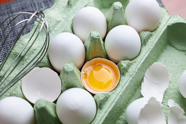 Groep van rauwe witte kippeneieren in Groenboeklade op houten tafel, vers half gebarsten ei en roestvrijstalen ei klop. Concept van een gezonde levensstijl.