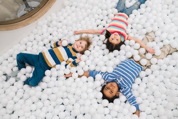 Groep van schattige interculturele lieve kinderen in vrijetijdskleding met plezier tijdens het spelen tussen witte ballonnen op de vloer