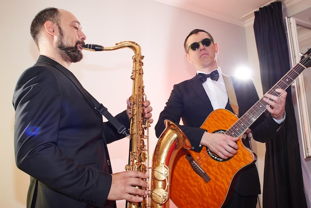 Groep van twee muzikanten, mannelijke jazzband, gitarist en saxofonist in klassieke kostuums improviseren op muziekinstrumenten in een studio podiumverlichting