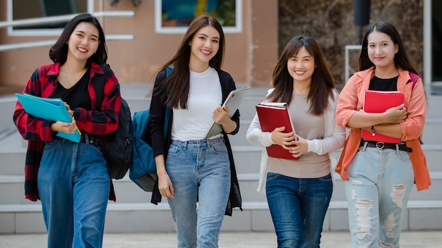 Groep van vier jonge, aantrekkelijke Aziatische meisjesstudenten die samen op de universiteitscampus lopen, pratend en lachend van vreugde. Concept voor onderwijs en studentenleven.