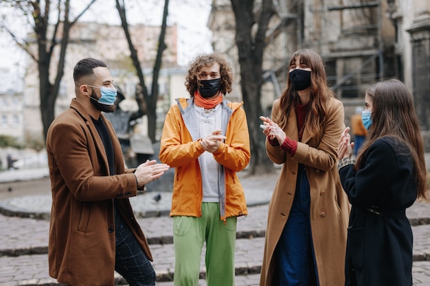 Groep van vier jonge mensen die ontsmettingsmiddel gebruiken en medische gezichtsmaskers dragen tijdens een ontmoeting tijdens het coronavirus. Concept van preventie en bescherming.