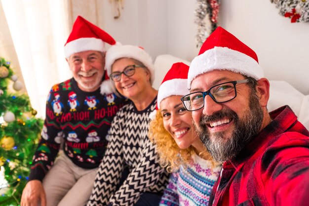 Groep van vier mensen glimlachen en kijken naar de camera van de jonge man die de camera vasthoudt - familie selfie thuis de kerstdag samen