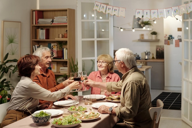 Groep van vier senior gelukkige vrienden rammelende met glazen wijn boven tafel