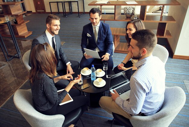 Groep van vijf jonge mensen die iets bespreken terwijl ze samen op kantoor aan tafel zitten