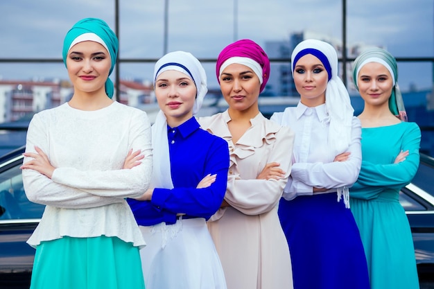 Groep van vijf sterke mooie en jonge moslim zakelijke vrouwen mode look stijlvolle lange jurk en de tulband bedekt het hoofd staande krachtig trots, auto en wolkenkrabber straat achtergrond