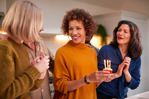 Groep volwassen vrienden die thuis samenkomen om de verjaardag van de vrouw met taart te vieren