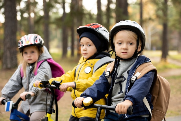 Groep vriendelijke kleine kinderen in vrijetijdskleding en beschermende helmen die op hun loopfietsen voor de camera zitten terwijl ze chillen in het openbare park
