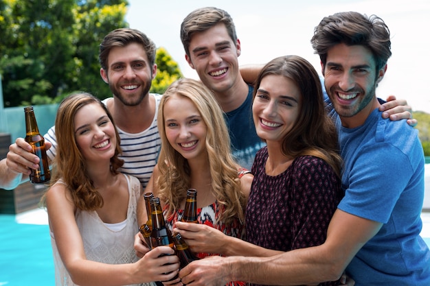 Groep vrienden die bierflessen roosteren dichtbij pool