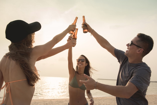 Groep vrienden die flessen van het partij claging bier hebben bij het strand