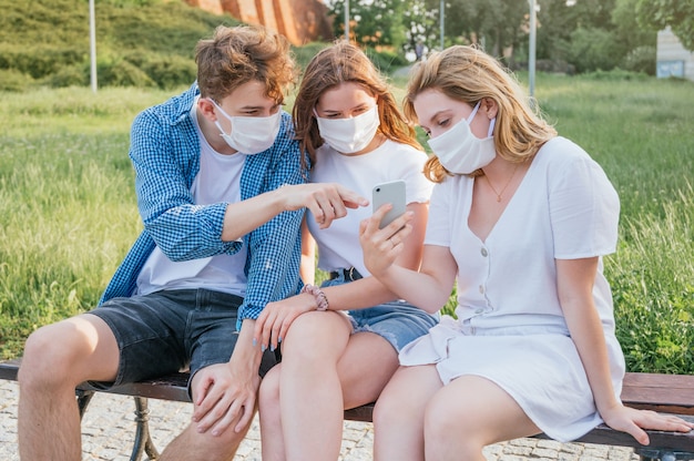 Groep vrienden die gezichtsmaskers dragen en op een smartphone letten