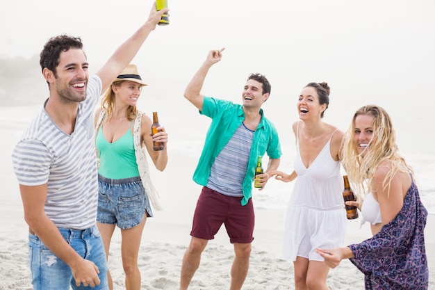 Groep vrienden die op het strand met bierflessen dansen