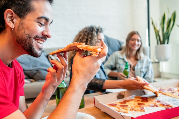 Foto groep vrienden die plezier hebben terwijl ze pizza eten en samen bier drinken.