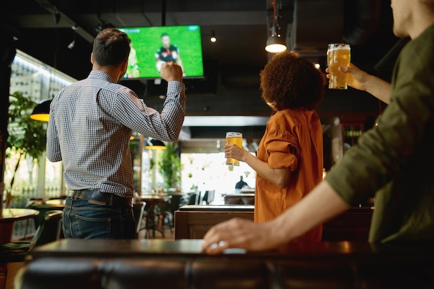 Groep vrienden kijken naar voetbalwedstrijd op tv-scherm en tapbier drinken. Jongeren rusten uit in sportbar of pub