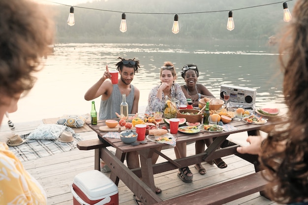 Groep vrienden zitten aan de tafel en eten hebben ze een picknick buitenshuis