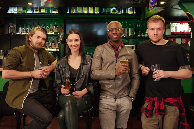 Groep vrienden zitten aan de toog met bier en glimlachen naar de camera in de pub