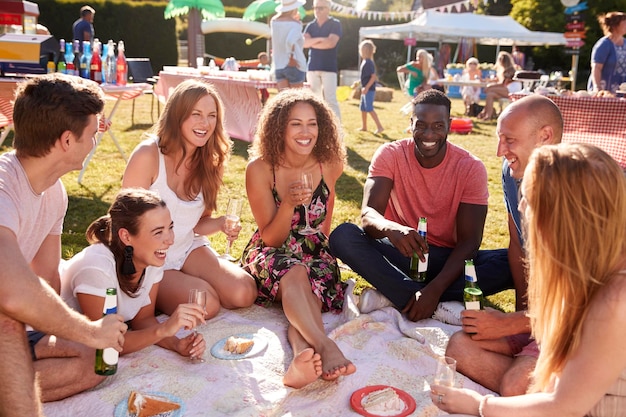 Groep vrienden zittend op tapijt op zomertuinfeest met drankjes