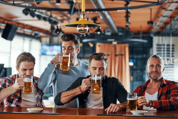 Groep vrolijke jonge mannen in casual kleding die van bier genieten terwijl ze aan de bar in de pub zitten